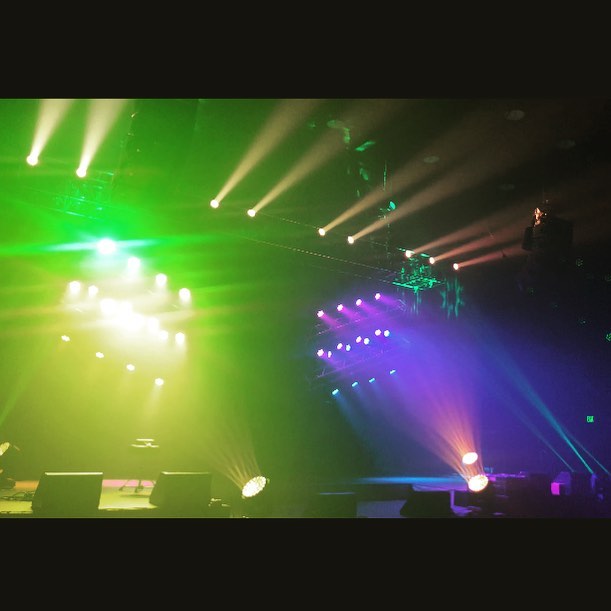 A green-and-violet lighting look washing over a concert stage