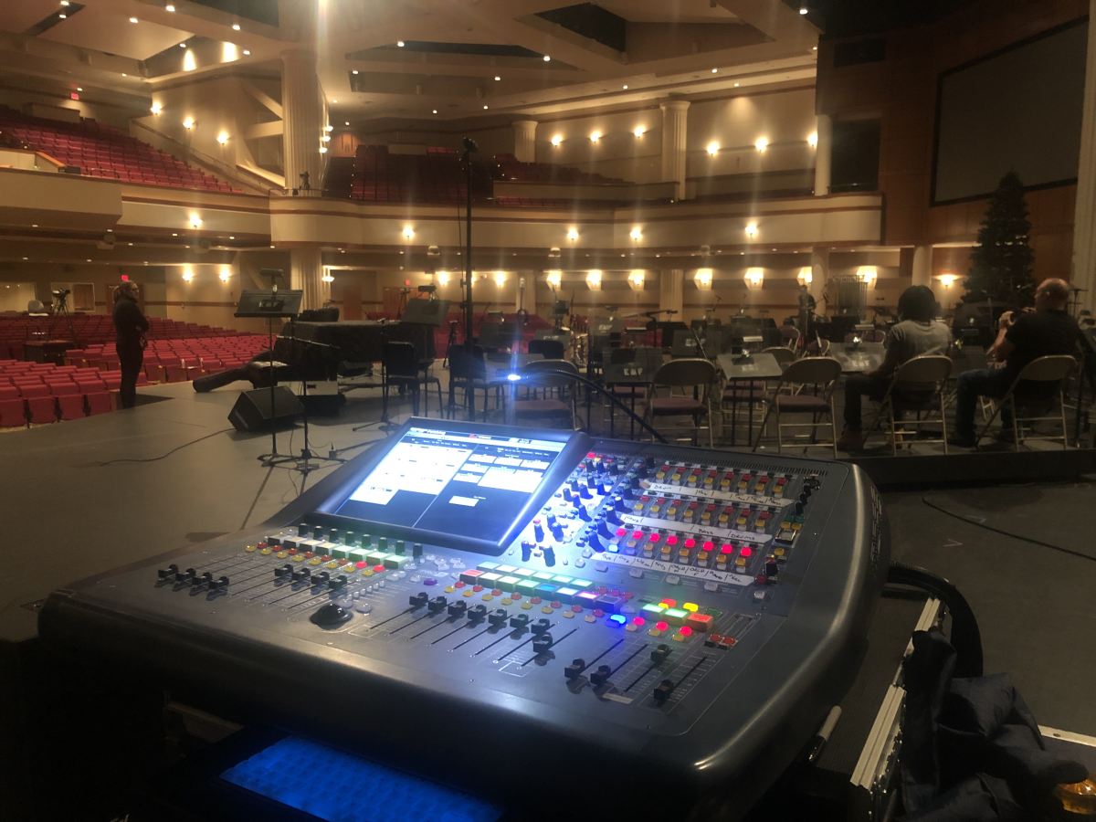 Solidus79 at front-of-house running a digital mixing console during a live rehearsal in a full auditorium